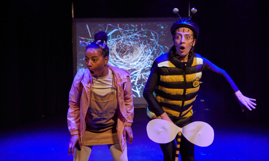 Two performers on stage with their mouths open in surprise, one is dressed as a bee.