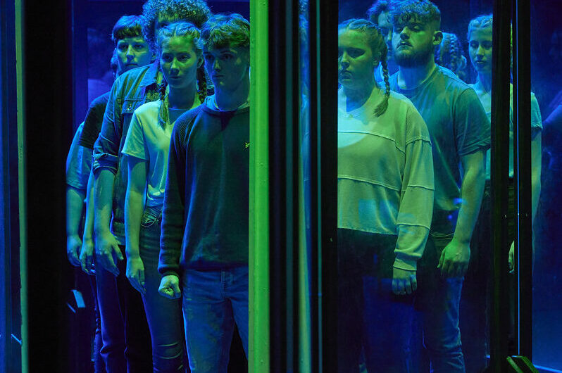 students washed in green and blue light stand behind a glass pane