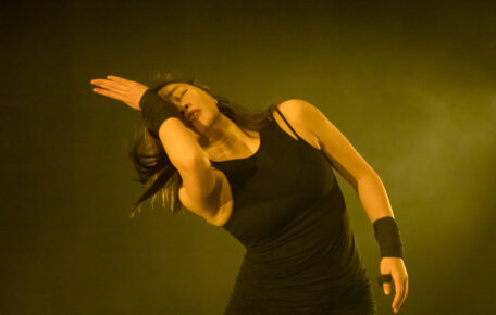 A dancer dressed in black with their hand over their face