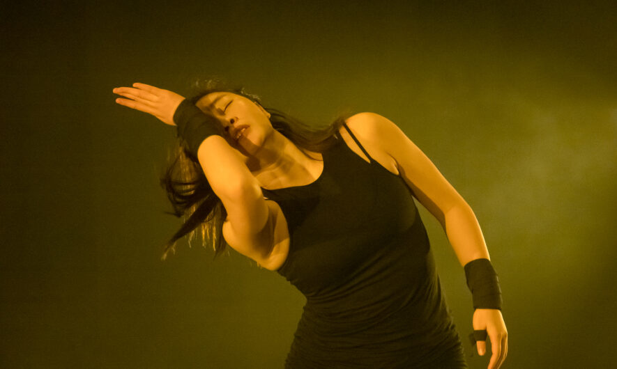A dancer dressed in black with their hand over their face