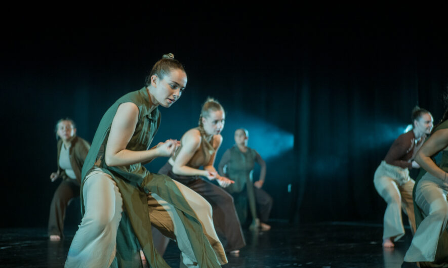 Dancers on stage in green costume squatting slightly.