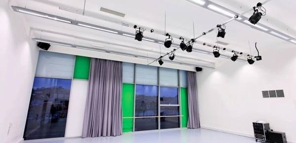 empty dance studios , lighting rig and windows are visible in this image. The space is white with grey floors.
