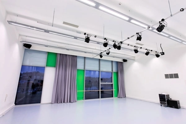empty dance studios , lighting rig and windows are visible in this image. The space is white with grey floors.