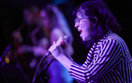 Performer sings into a micropone washed in pink light.