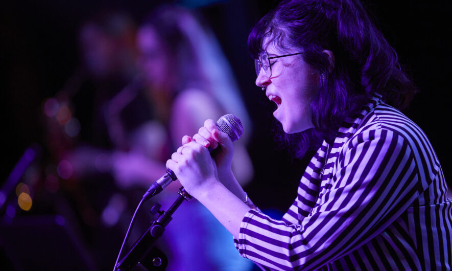 Performer sings into a micropone washed in pink light.