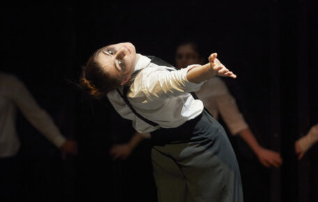 A dancer leans back and holds their hand out.