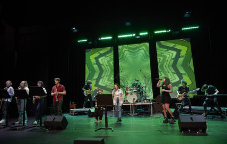 Singers standing on a stage with green light screen behind them
