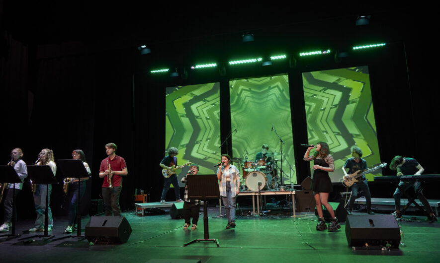Singers standing on a stage with green light screen behind them