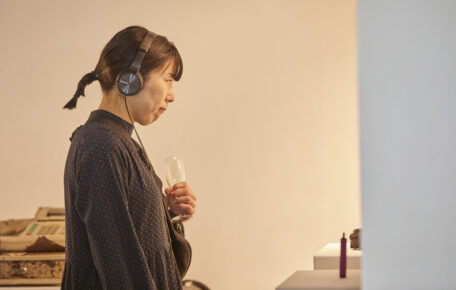 Person holding a drink looking at artwork with headphones on.