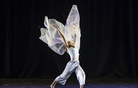 Dancer surrounded by fabric throwing it into the air on a black background.