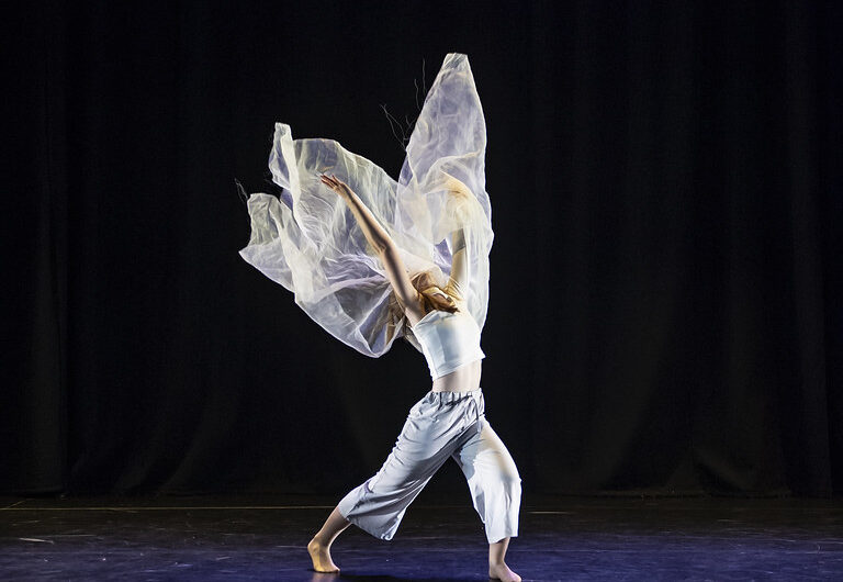 Dancer surrounded by fabric throwing it into the air on a black background.