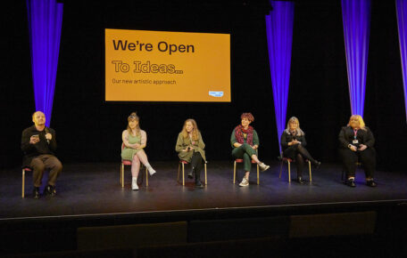 Lincoln Arts Centre team on stage sitting on chairs with presentation behind reading 'we're open to ideas'