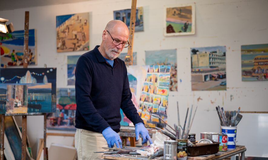 Man in a artists workshop. There paintings on the wall behind him.