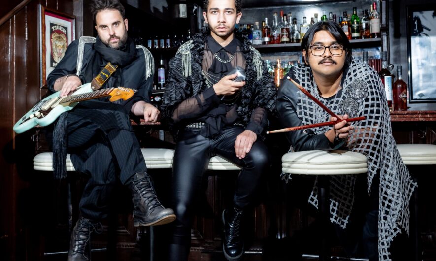 3 people leaning on bar stalls holding musical instruments. Wearing rock n roll style clothing.