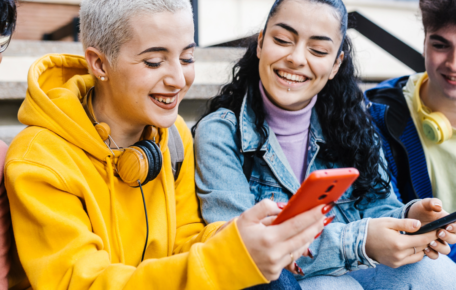Two young people look at a phone and smile.
