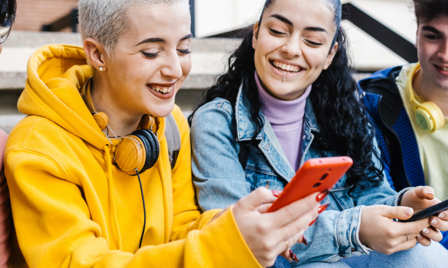 Two young people look at a phone and smile.