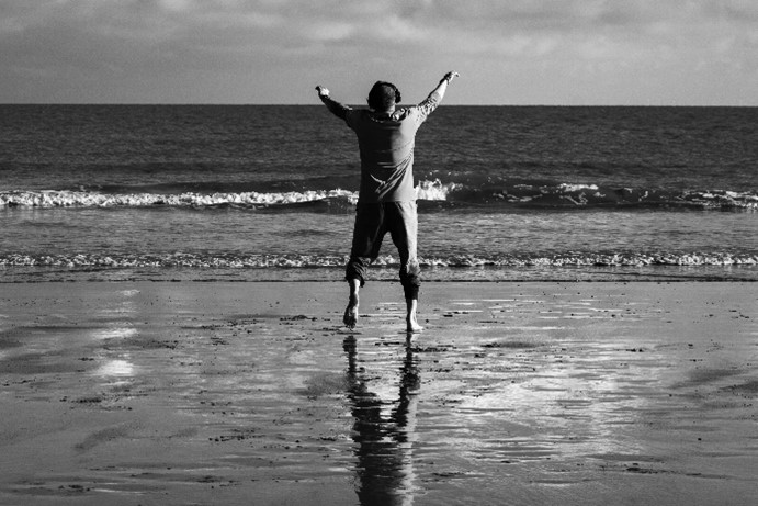 Black and white photo of a person standing at the shore on the beach.