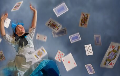 Alice is falling through a blue smokey background, several playing cards fall with her of various suits and numbers.