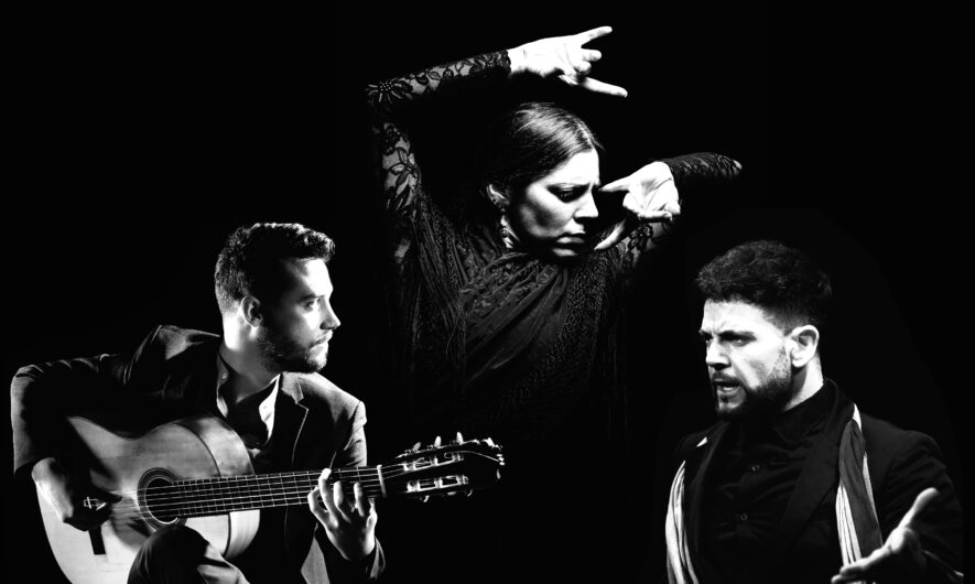 Vlack and white image of three people. On the left, one is playing guitar, whilst the other two dance.