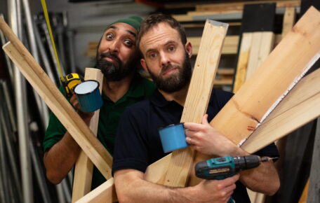 Two men holding wooden planks and mugs.