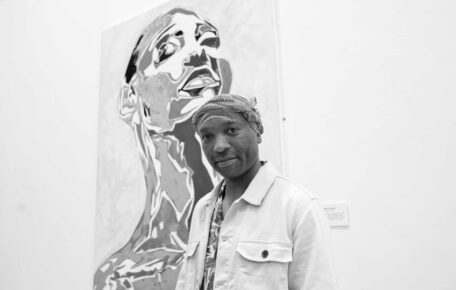 Black and white photo of Tinashe in front of one of his paintings in the gallery.