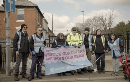 A Rubbish Documentary | Short Film. Screengrab from the documentary. Shows a group of people at Sincil Bank in Lincoln holding a banner which reads 'Let's rescue our rivers and save our seas'.