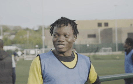 Screen shot from the Kicking Off documentary shows a young player with dark hair smiling. He wears a bright yellow tricot and blue vest.