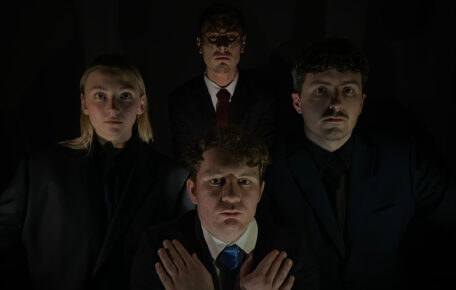 Promotional image for student Cabaret, 4 actors face forward, wearing smart clothes against a dark background