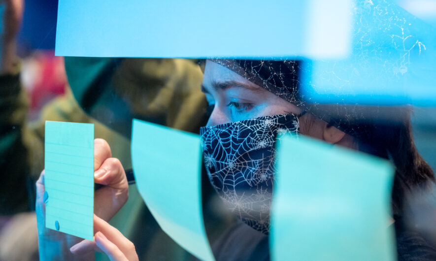 Post it notes on a glass wall and woman writing down on one of them
